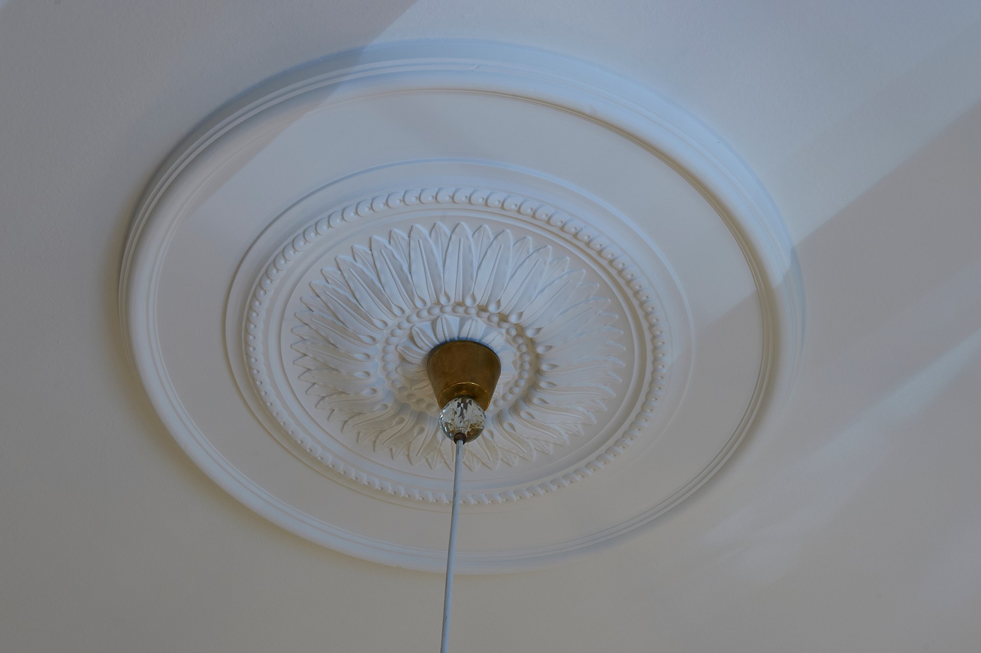 Rosace décorative au relief finement travaillé, qui met en valeur une suspension dans un plafond au design raffiné.